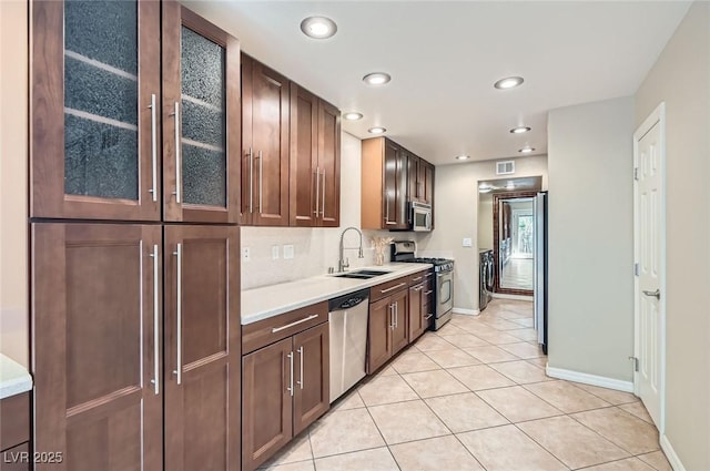 kitchen featuring stainless steel appliances, a sink, baseboards, light countertops, and glass insert cabinets