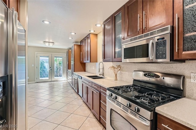 kitchen featuring stainless steel appliances, a sink, french doors, light tile patterned flooring, and glass insert cabinets
