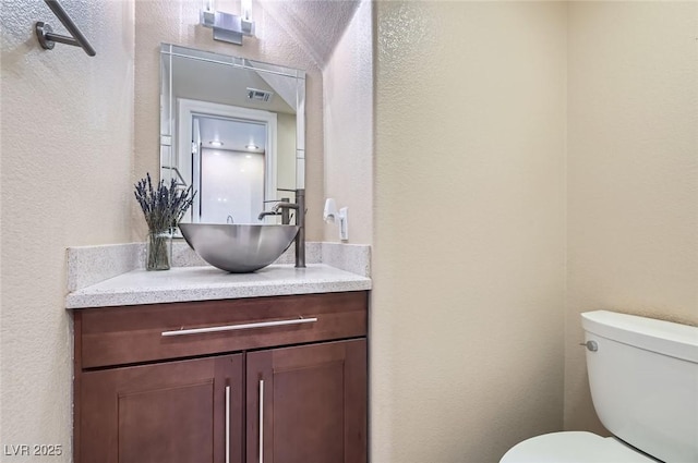 bathroom featuring a textured wall, toilet, and vanity