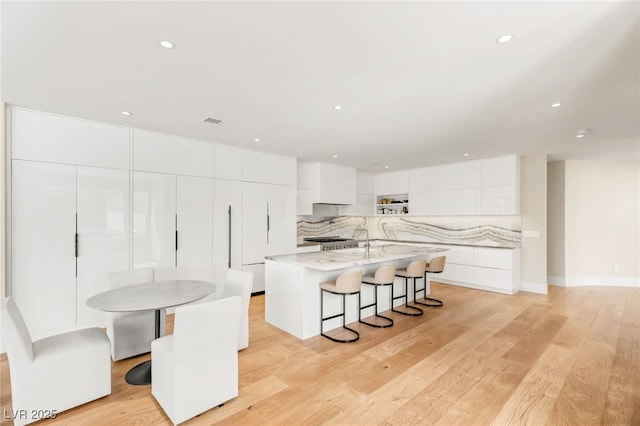 11453 Glowing Sunset Ln, Las Vegas, NV 89135 - kitchen featuring modern cabinets, backsplash, white cabinetry, a kitchen bar, and a kitchen island with sink