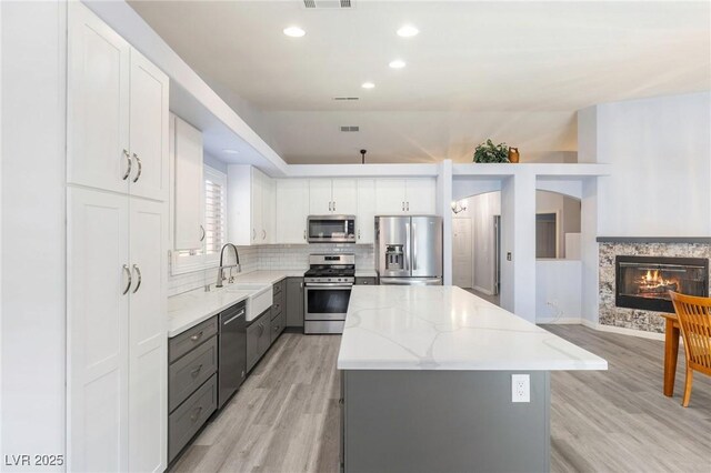5441 Rose Hills St, Las Vegas, NV 89149 - kitchen with appliances with stainless steel finishes, a sink, light wood-type flooring, a kitchen island, and light stone counters