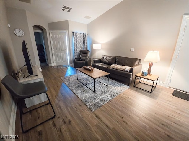 living room with arched walkways, wood finished floors, baseboards, and lofted ceiling