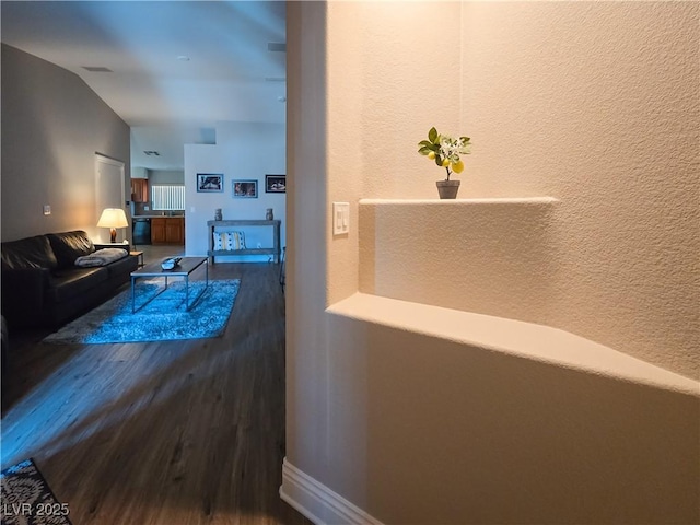 hallway with lofted ceiling, wood finished floors, baseboards, and a textured wall