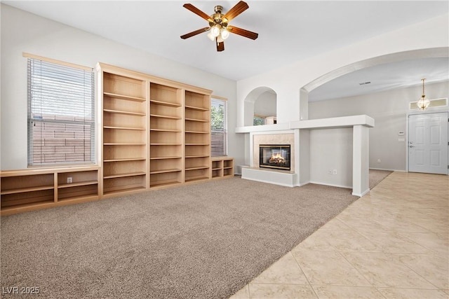 9282 W Viking Rd, Las Vegas, NV 89147 - unfurnished living room featuring ceiling fan, a tiled fireplace, tile patterned floors, arched walkways, and carpet flooring