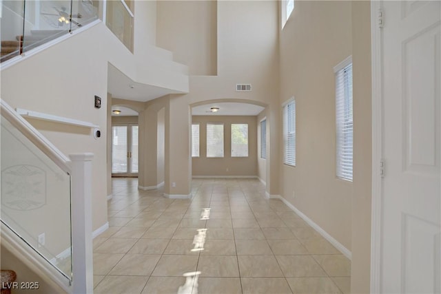 entryway featuring arched walkways, light tile patterned flooring, baseboards, and a towering ceiling