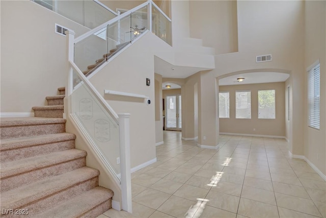 staircase featuring arched walkways, a towering ceiling, tile patterned floors, and baseboards