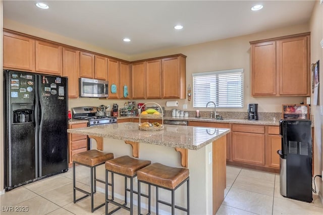 kitchen with appliances with stainless steel finishes, a sink, light tile patterned floors, a center island, and light stone countertops