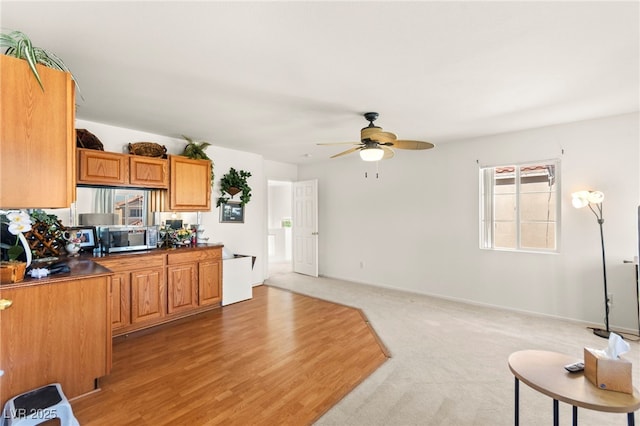 9522 Arrowhead Falls Ct, Las Vegas, NV 89148 - kitchen with stainless steel microwave, ceiling fan, brown cabinetry, baseboards, and light carpet