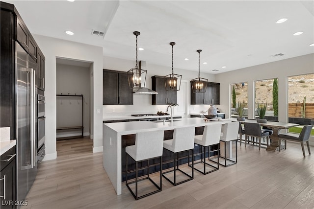 2601 Nevada Agave Ln, Las Vegas, NV 89138 - kitchen with light countertops, a breakfast bar, recessed lighting, wall chimney exhaust hood, and a center island with sink