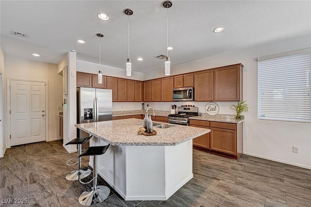 8164 Golden Cholla Ave, Las Vegas, NV 89179 - kitchen featuring stainless steel appliances, a sink, brown cabinets, a kitchen island with sink, and recessed lighting