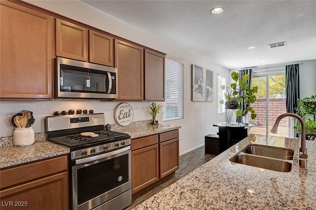 8164 Golden Cholla Ave, Las Vegas, NV 89179 - kitchen featuring stainless steel appliances, a sink, light stone countertops, brown cabinets, and baseboards
