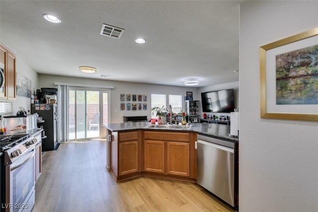 kitchen featuring appliances with stainless steel finishes, dark countertops, light wood-style floors, a sink, and brown cabinetry