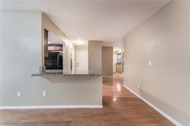 1729 Yellow Rose St, Las Vegas, NV 89108 - kitchen with freestanding refrigerator, light wood finished floors, a textured ceiling, baseboards, and a peninsula