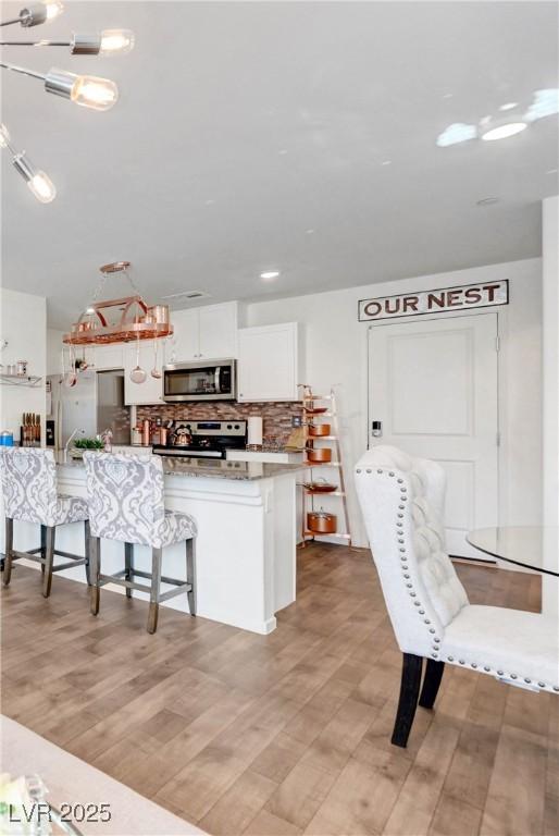1125 Meadow Sparrow Pl, Henderson, NV 89011 - kitchen with stainless steel appliances, light wood-style floors, white cabinetry, a kitchen breakfast bar, and decorative backsplash