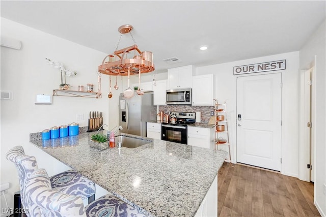 1125 Meadow Sparrow Pl, Henderson, NV 89011 - kitchen with stainless steel appliances, a peninsula, a sink, white cabinetry, and wood finished floors
