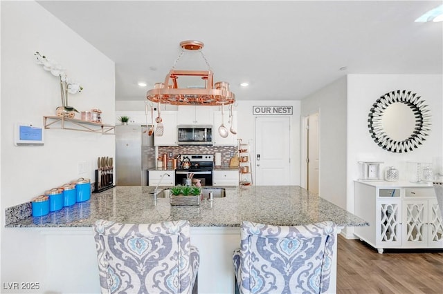 1125 Meadow Sparrow Pl, Henderson, NV 89011 - kitchen featuring appliances with stainless steel finishes, decorative backsplash, wood finished floors, light stone counters, and a peninsula