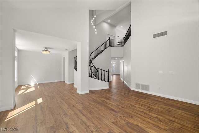 4607 El Camino Cabos Dr, Las Vegas, NV 89147 - unfurnished living room featuring stairway, wood finished floors, a towering ceiling, arched walkways, and baseboards