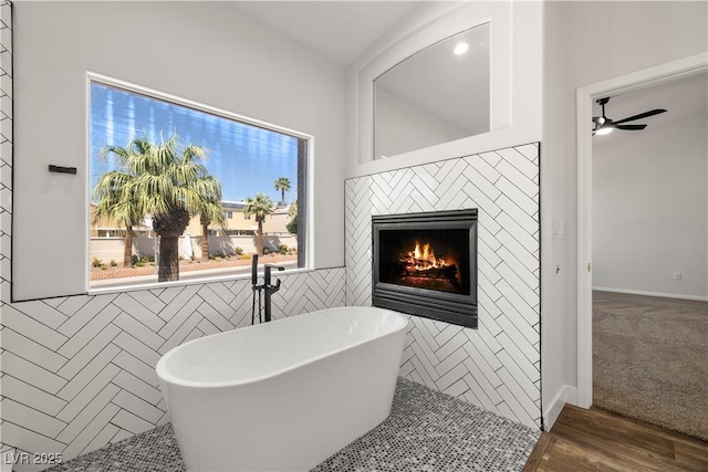4607 El Camino Cabos Dr, Las Vegas, NV 89147 - full bathroom featuring a lit fireplace, a soaking tub, a ceiling fan, tile walls, and wood finished floors