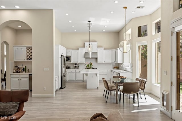801 Aquitaine Ct, Las Vegas, NV 89145 - kitchen featuring appliances with stainless steel finishes, a towering ceiling, a kitchen island, light wood-style floors, and white cabinetry