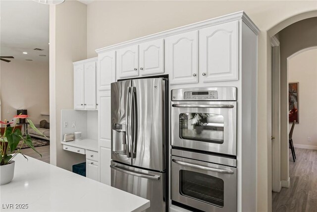 801 Aquitaine Ct, Las Vegas, NV 89145 - kitchen with appliances with stainless steel finishes, arched walkways, light wood finished floors, white cabinets, and light countertops