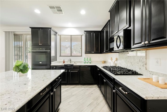 kitchen featuring dark cabinetry, black appliances, a sink, light stone counters, and recessed lighting