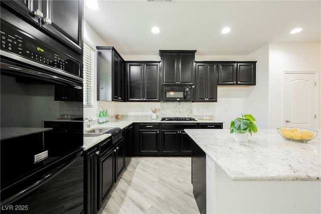 kitchen featuring black appliances, dark cabinetry, a sink, light stone countertops, and backsplash