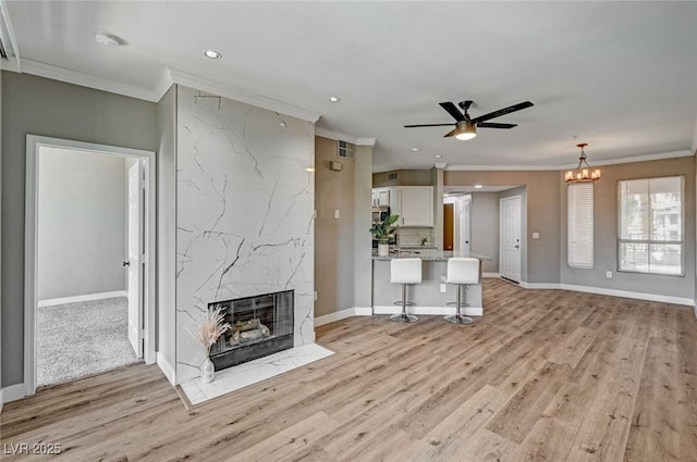 unfurnished living room featuring ornamental molding, a ceiling fan, a premium fireplace, light wood finished floors, and recessed lighting
