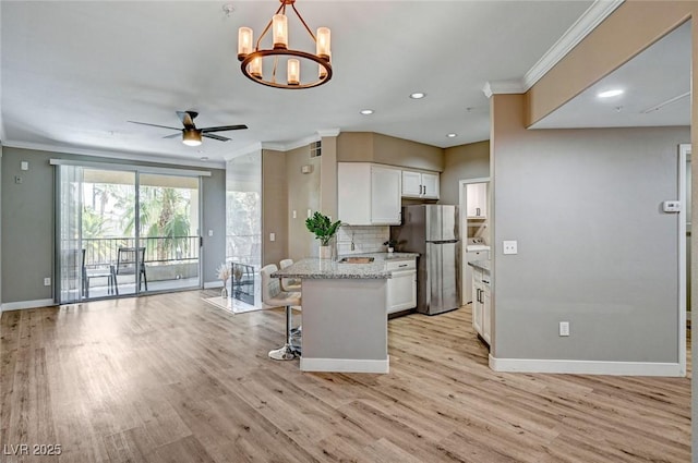 kitchen featuring freestanding refrigerator, ornamental molding, baseboards, white cabinetry, and a kitchen bar