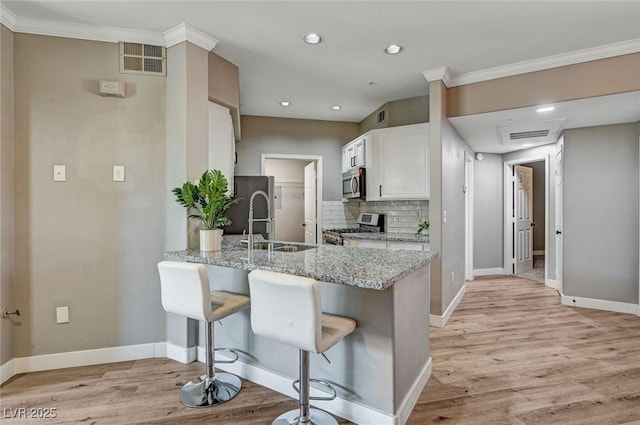 kitchen featuring stainless steel appliances, ornamental molding, tasteful backsplash, light stone countertops, and a peninsula