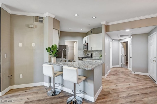kitchen with appliances with stainless steel finishes, light stone counters, a peninsula, a sink, and white cabinets