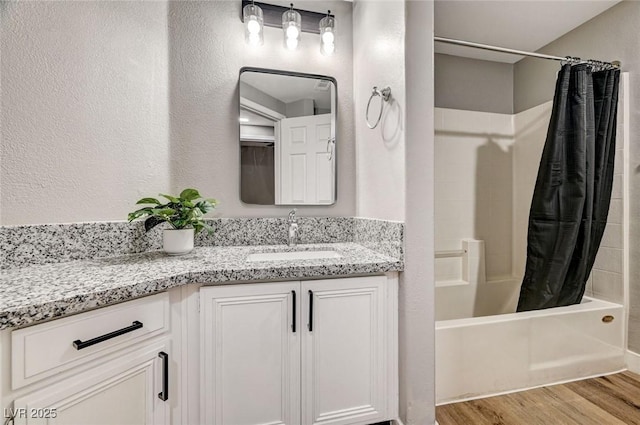 bathroom featuring wood finished floors, shower / tub combo, vanity, and a textured wall