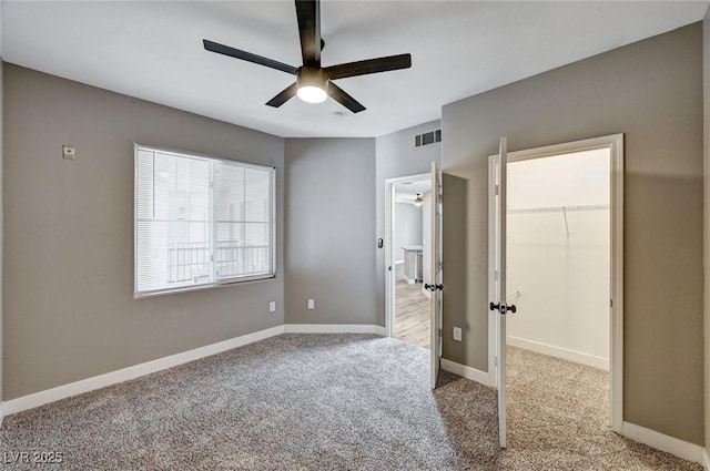 unfurnished bedroom with carpet, a walk in closet, a ceiling fan, a closet, and baseboards