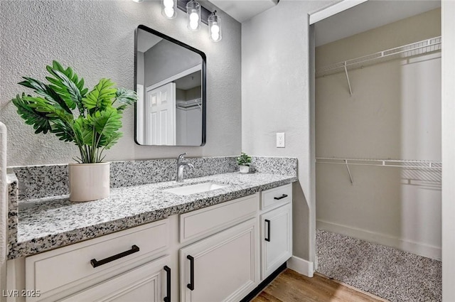 bathroom with wood finished floors, vanity, a spacious closet, and a textured wall