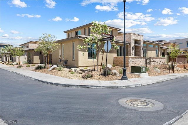 view of front of house featuring stucco siding, a residential view, fence, and stone siding