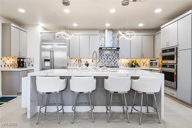 kitchen with stainless steel appliances, wall chimney exhaust hood, decorative backsplash, light countertops, and a breakfast bar area