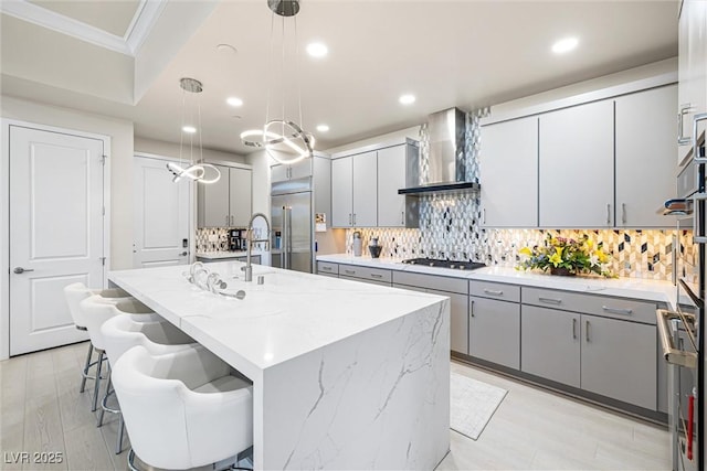 kitchen featuring wall chimney exhaust hood, stainless steel built in refrigerator, gray cabinets, oven, and ornamental molding