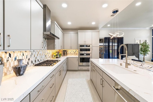 kitchen featuring stainless steel appliances, wall chimney exhaust hood, recessed lighting, a sink, and pendant lighting