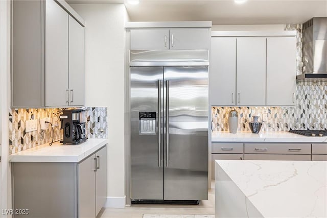 kitchen featuring appliances with stainless steel finishes, gray cabinetry, wall chimney exhaust hood, tasteful backsplash, and light stone countertops