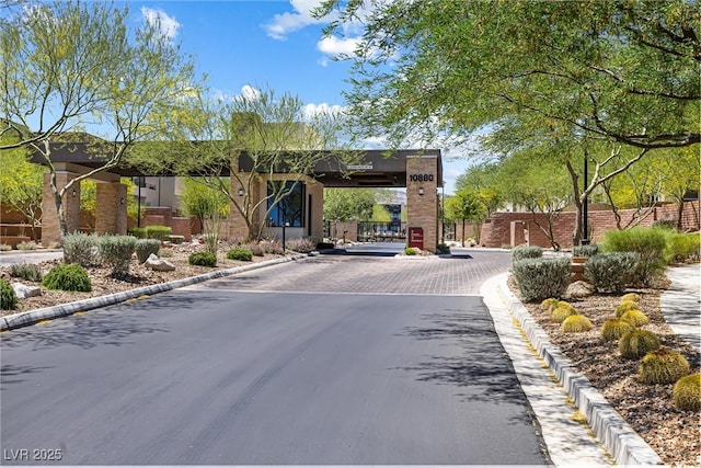 view of asphalt road featuring curbs, a gate, and a gated entry
