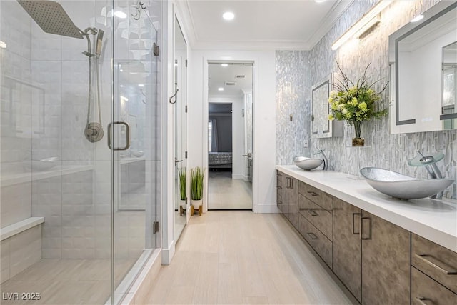 bathroom with crown molding, a stall shower, wood finished floors, double vanity, and recessed lighting