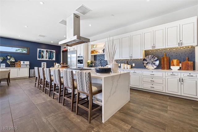 kitchen with stainless steel appliances, island exhaust hood, white cabinets, a center island, and tasteful backsplash