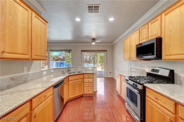 kitchen with stainless steel appliances, a sink, light wood-style flooring, light brown cabinets, and ornamental molding