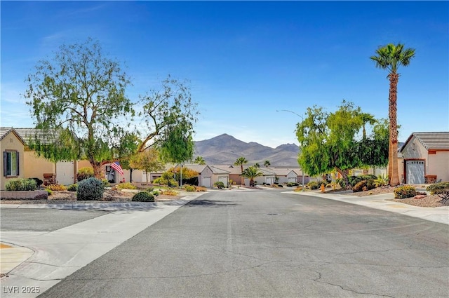 view of asphalt road featuring a residential view, a mountain view, street lighting, and sidewalks