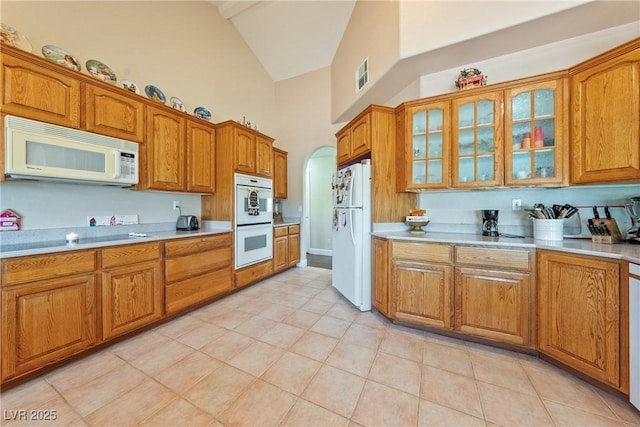3640 E Vineyard Dr, Pahrump, NV 89048 - kitchen with white appliances, high vaulted ceiling, brown cabinets, light countertops, and glass insert cabinets