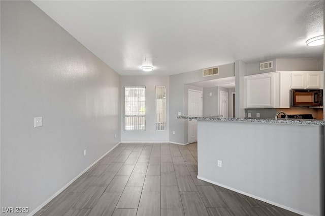 7189 S Durango Dr Unit 208, Las Vegas, NV 89113 - kitchen with black microwave, white cabinetry, baseboards, and light stone counters
