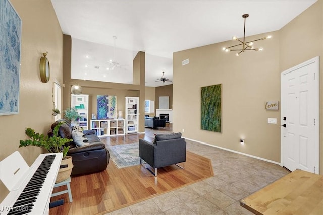 living area with a ceiling fan, high vaulted ceiling, a chandelier, baseboards, and tile patterned flooring