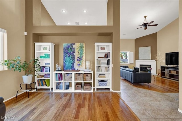 living room featuring lofted ceiling, a ceiling fan, wood finished floors, a glass covered fireplace, and recessed lighting