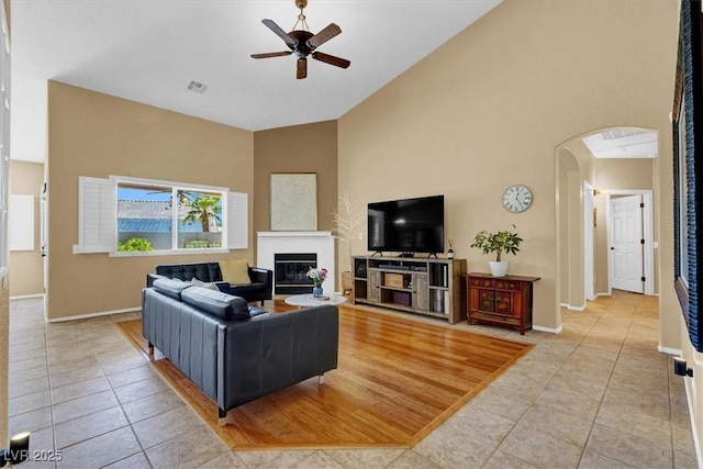 living area featuring ceiling fan, light tile patterned floors, high vaulted ceiling, arched walkways, and baseboards