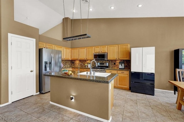 kitchen with appliances with stainless steel finishes, high vaulted ceiling, tasteful backsplash, an island with sink, and a sink