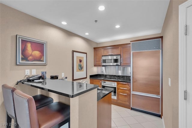 135 E Harmon Ave Unit 1102, Las Vegas, NV 89109 - kitchen featuring stainless steel appliances, brown cabinetry, a peninsula, dark countertops, and a breakfast bar area